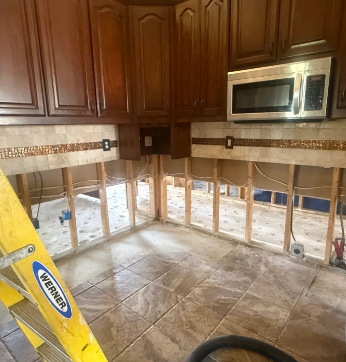 A kitchen with dark wood cabinets and a stainless steel microwave under demolition